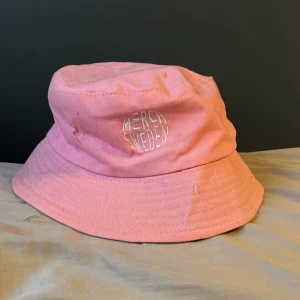 Rosa bucket hat från Merch Sweden. Signerad av Fredde  - Snygg rosa bucket hat från Merch Sweden med broderad vit logga framtill. Klassisk form med bred brätte och tillverkad i bomull. Perfekt accessoar för att lyfta din stil och ge en cool vibe till outfiten.Den är signerad av Fredde och är helt oanvänd 