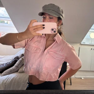 Croppad rosa denimskjorta - Säljer en croppad skjorta i ljusrosa denim med korta ärmar. Skjortan har klassisk krage och en loose passform som ger en avslappnad vibe💖använd fåtal gånger