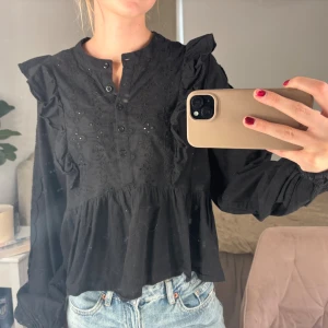 Svart blus med volang från Bikbok - Svart blus från Bikbok med broderade detaljer och volanger på axlarna.