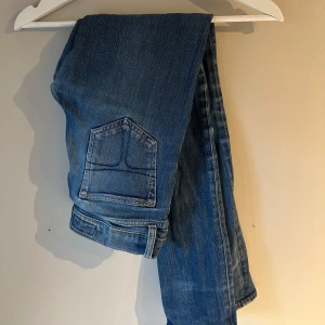 Blå jeans från Tiger of Sweden - Säljer ett par klassiska blå jeans från Tiger of Sweden. Jeansen har raka ben, normal passform och snygga detaljer på bakfickorna. Tillverkade i slitstarkt denimtyg som ger en tidlös look. Perfekta för dig som gillar stilrena och enkla jeans.