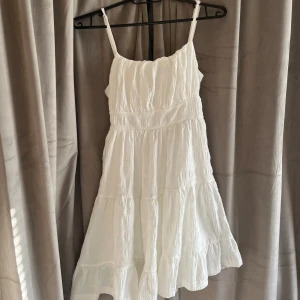 Vit somrig kortklänning med volang - Superfin vit kortklänning med tunna axelband och volangig kjol. Klänningen har en lätt rynkad struktur och smock i ryggen för extra komfort. Perfekt för varma dagar och ger en luftig känsla. Passar dig som gillar en enkel men söt stil. Hör av dig vid frågor!💕
