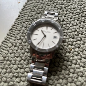 Silverfärgad klocka från Thomas Sabo - Stilren klocka från Thomas Sabo med rund urtavla i vitt och datumvisning. Klockan har en robust länkad armlänk i silverfärgat metall och tydliga indexmarkeringar. Perfekt accessoar för dig som gillar klassisk och tidlös design.