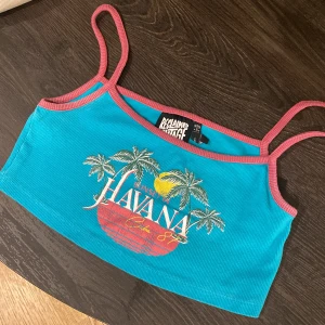 Turkos cropptopp från Reclaimed Vintage - Säljer en turkos cropptopp från Reclaimed Vintage med rosa kantband och smala axelband. Toppen har tryck med palmer, solnedgång och texten 'Havana'.