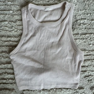 Beige ribbad croppad linnetopp - Säljer en stilren croppad linnetopp i beige med ribbad struktur. Toppen är ärmlös och har en klassisk rund halsringning. Perfekt för varma dagar eller att styla lager på lager. Materialet är mjukt och stretchigt för en bekväm passform.