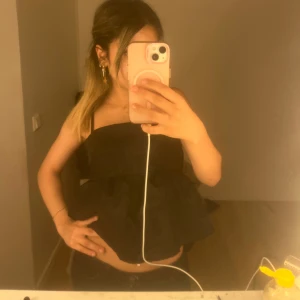 Svart volangig linnetopp med smala axelband - Säljer en svart linnetopp med smala axelband och volangig, luftig nederdel. Toppen har en rak skurning upptill och är croppad, vilket ger en trendig och avslappnad look. Perfekt att styla med jeans eller kjol!!💕💕🫰