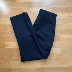 Svarta kostymbyxor från Zara - Snygga svarta kostymbyxor från Zara med klassisk rak passform. Byxorna har hällor för bälte, diskreta fickor och är tillverkade i ett mjukt tyg som känns bekvämt hela dagen. Perfekta för en stilren look.