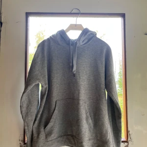 Grå hoodie från Jacqueline de Yong - Säljer en grå hoodie från Jacqueline de Yong i storlek S. Tröjan har huva med snörning, stor magficka och långa ärmar. Perfekt för chill dagar och enkel att matcha med jeans eller mjukisbyxor.