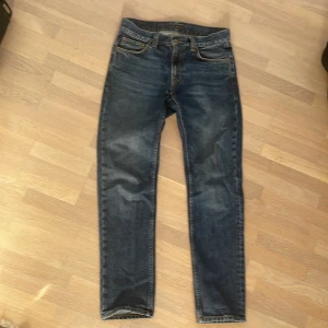 Nudie Jeans blå jeans 28/32 - Snygga blå jeans från Nudie Jeans i klassisk femficksmodell. Jeansen har en rak passform med normal midja och är tillverkade i slitstarkt bomullstyg. Bakfickorna har Nudies ikoniska broderade vågmönster och läderpatch i midjan.