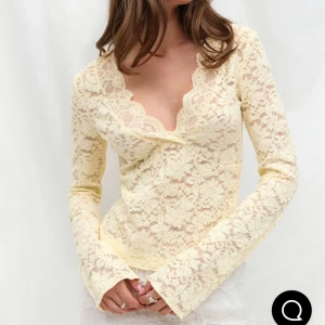 Krämvit spetsblus med v-ringning - Superfin krämvit blus från Gina Tricot i genombruten spets med blommigt mönster. Djup v-ringning med vågig kant och långa ärmar. Perfekt för dig som gillar romantisk och feminin stil. Blusen är figurnära och har en lätt croppad passform.