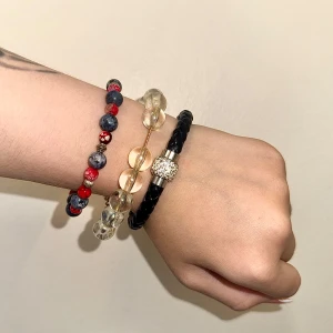 Tre armband med pärlor - Säljer tre snygga armband: ett med svarta och röda pärlor, ett med stora transparenta pärlor och ett flätat svart läderarmband med glittrig detalj. 