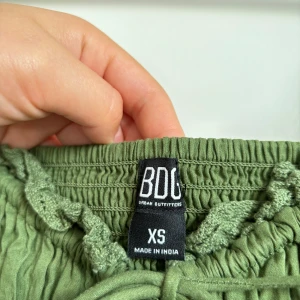 Bohemisk klänning från BDG Urban Outfitters, 100% bomull - Aldrig använd mellanlång olivgrön bohemisk klänning från BDG Urban Outfitters i storlek XS. Är 100% bomull. Nypris 700 kr. 