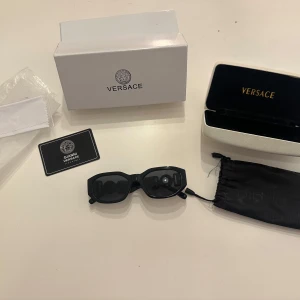 Svarta solglasögon från Versace - Snygga svarta solglasögon från Versace med rektangulära bågar och ikoniska guldfärgade Medusa-detaljer på sidorna. Perfekt accessoar för en lyxig och trendig look.