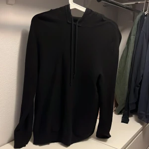 Svart stickad hoodie  - En stilren svart hoodie med huva och snörning. Den är i storlek xs. Väldigt bekväm . Skicket är relativt bra det är inte ny men ser fortfarande bra ut. Det finns ett hål i högra armhålan ganska litet( se på bild tre) skriv vid frågor eller funderingar.