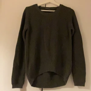 Mörkgrön stickad tröja - Mysig mörkgrön stickad tröja med rund halsringning och lång ärm. Tröjan har en något längre bakdel vilket ger en snygg och avslappnad look. Perfekt för kyliga dagar och enkel att matcha med jeans eller kjol.