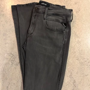 Gråa Replay jeans  - Säljer ett par helt nya gråa Replay jeans i slim fit-modell i storlek 33/34. Byxorna har klassisk femficksdesign, dragkedjegylf och svarta detaljer. Snygg tvätt och stretchigt material som sitter tajt men bekvämt. Perfekta för dig som gillar stilrena och moderna jeans.