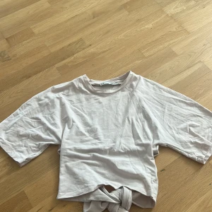 Ljusrosa knyt-topp från lager 157 - Säljer en ljusbeige topp från 15DE i storlek M. Toppen har korta, vida ärmar och en snygg knyt-detalj framtill som ger en trendig look. Tillverkad i mjuk bomull, perfekt för en chill och avslappnad stil.