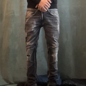 Svarta slitna jeans från Dondup - Säljer ett par svarta jeans från Dondup med coola slitningar och trasiga detaljer på benen. Jeansen har en smal passform och klassiska fem fickor. Snyggt tvättade med grå och svarta nyanser storlek 29.skickar endast med postnord 