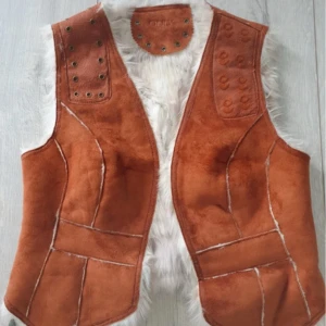 Brun pälsväst från ONLY, stl M - Säljer en brun pälsväst från ONLY med vit fluffig fuskpäls på insidan. Västen har dekorativa nitar på axlarna och coola synliga sömmar. Perfekt för dig som vill ha en boho-vibe och sticka ut lite extra.