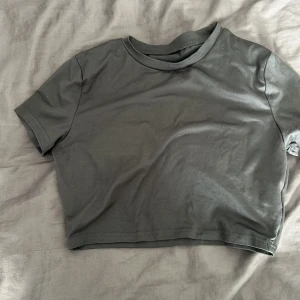 Svart croppad topp från SHEIN - En enkel grå/svart croppad topp från SHEIN med rund halsringning och korta ärmar. Tillverkad i mjuk och stretchig polyesterblandning som sitter snyggt på kroppen. Perfekt att matcha med jeans eller kjol för en clean look.