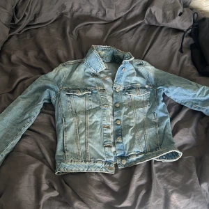 Ljusblå jeansjacka från Zara, M - Snygg ljusblå jeansjacka från Zara i klassisk modell med knappar framtill och två bröstfickor med lock. Jackan har raka sömmar, krage och är tillverkad i slitstarkt denim. Perfekt för dig som vill ha en tidlös och ren look.