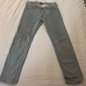 Grå Lee jeans straight fit - Snygga grå jeans från Lee med klassisk femficksdesign och raka ben. Jeansen har Lee-logga på bakfickan och metallknapp framtill. Perfekta för dig som gillar en enkel och stilren look. Materialet är slitstarkt denim i bomull. Bara lite urtvättade men de ger den ett härligt mönster utan tecken på skador!