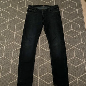 Mörkblå skinny jeans från Lee - Säljer ett par mörkblå skinny jeans från Lee med klassiska gula sömmar och läderpatch bak. Jeansen har fem fickor och är tillverkade i stretchigt denim för en tight passform. Perfekta för dig som gillar en stilren och enkel look.