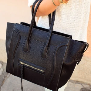 Svart handväska i skinn med dragkedja ”must have bag” - Stilren svart handväska i skinnimitation med två rejäla handtag och snygga detaljer. Väskan har en praktisk dragkedja framtill med flätad tofs och breda sidor som ger extra utrymme. 