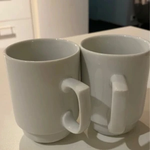 Två vita porslinsmuggar - Två stilrena vita porslinsmuggar i klassisk design. Perfekta för kaffe eller te. Muggarna är i mycket gott skick utan synliga repor eller sprickor. Passar både till vardag och fest. Säljes i par.