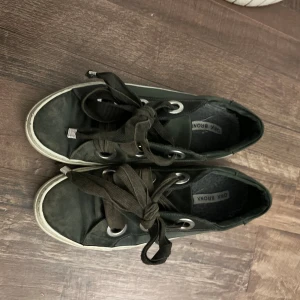 Svarta sneakers från Onx Bronx - Säljer ett par svarta sneakers från Onx Bronx med breda svarta snören och silvriga metalldetaljer vid snörningen. Skorna har en vit platt sula och rund tå. Perfekta för dig som gillar en enkel men cool stil.