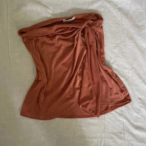 tubtopp från NLY One - Säljer en snygg coral tubtopp från NLY One i storlek M. Toppen är axelbandslös och har en draperad omlott-look framtill som ger en cool och trendig vibe. Perfekt att styla med jeans eller kjol för en modern look.