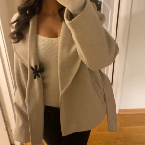 Beige kappa från Vero Moda med bälte - Säljer en snygg beige kappa från Vero Moda i storlek S. Jackan har bred krage, bälte i midjan. Materialet känns mjukt och är super varm till vinter! Storleken är ganska stor. Pris kan diskuteras! (Köptes för 599kr) 