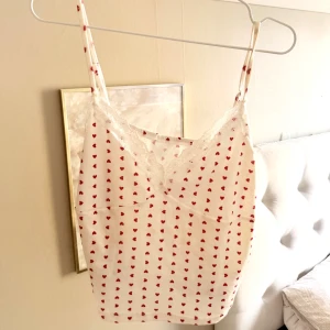 Vit linnetopp med röda hjärtan och spets - Supersöt vit linnetopp med röda hjärtan och tunna axelband. Toppen har v-ringning med vit spetskant och är figurnära i modellen. Perfekt för dig som gillar gulliga detaljer och romantisk stil. Fel storlek för mig 