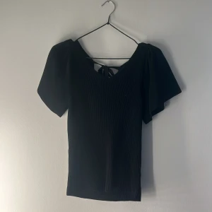 Svart ribbad topp från ONLY - Svart ribbad topp från ONLY med v-ringning, korta puffärmar och snygg knytning i ryggen. Väldigt fin och elegant. Använd fåtal gånger. Pris kan diskuteras💕