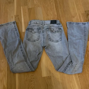 Grå bootcut jeans från Perfect Jeans - Snygga grå jeans från Perfect Jeans i storlek 32. Modellen har bootcut-ben och klassisk femficksdesign med detaljerade bakfickor och knappstängning. Jeansen har en cool tvättad look och passar dig som gillar lite bredare ben. Perfekt för dig som vill ha en avslappnad stil.