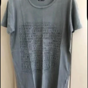 Grå t-shirt med tryck ny  - Snygg grå t-shirt med korta ärmar och rund hals. Framsidan har ett coolt texttryck i mörkare grått som ger en urban vibe. Perfekt basic-plagg i mjuk bomull som funkar till det mesta. Enkel och stilren design.