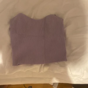 Ljuslila ribbad tubtopp S - Superfin ljuslila ribbad tubtopp i stickad känsla. Toppen är bandeau-modell och sitter tight mot kroppen. Perfekt att styla med jeans eller kjol för en trendig look.