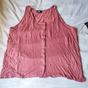 Rosa linnetopp med knappar från Boohoo - Säljer en rosa ärmlös linnetopp från Boohoo i storlek XS. Toppen har rund halsringning och knappar hela vägen framtill. Tillverkad i mjuk bomull, perfekt för varma dagar. Enkel och snygg modell som är lätt att matcha.