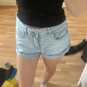 Ljusblå jeansshorts från H&M - Säljer ett par ljusblå jeansshorts från H&M i storlek 34. De har klassisk femficksdesign, upprullade benslut och normal passform. Perfekta för varma dagar och enkla att matcha med allt. Snygga och bekväma shorts för dig som gillar en avslappnad stil.