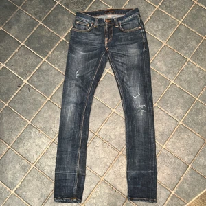 Mörkblå skinny jeans från Nudie Jeans - Snygga mörkblå skinny jeans från Nudie Jeans med klassisk femficksdesign och slitna detaljer. Jeansen har kontrastsömmar, läderpatch bak och subtila tvättade effekter. Perfekt passform för dig som gillar en tight look.