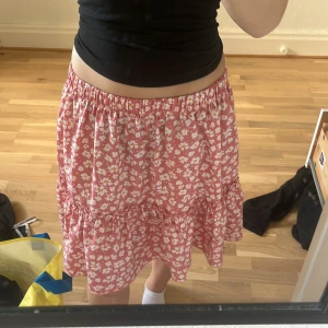 Rosa blommig volangkjol från SHEIN - Supersöt rosa kortkjol från SHEIN med vitt blommönster och volangdetaljer. Kjolen har resår i midjan för en bekväm passform och är perfekt för en somrig look. Tillverkad i lätt polyester som känns luftig och skön.