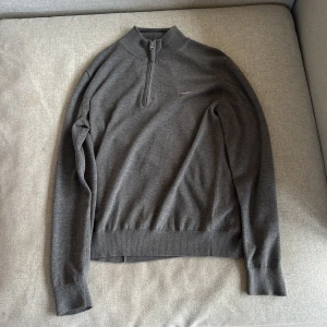 Grå half zip tröja  - Snygg grå långärmad tröja från GANT med broderad logga på bröstet. Tröjan har en ribbad krage och muddar samt en praktisk half zip-dragkedja. Perfekt för lager-på-lager och passar till många olika stilar. Passar dig runt 170