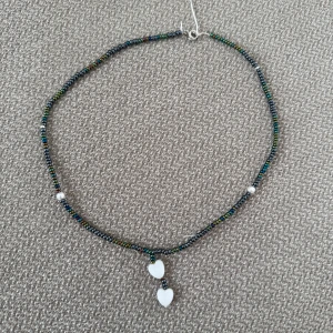 Färgglatt pärlhalsband med hjärtan - Pärlhalsband med små pärlor i regnbågsfärger och två vita hjärtformade pärlor som hänge, det är 37cm långt 🖤🤍💚