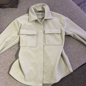 Ljusgrön overshirt från Gina Tricot - Snygg ljusgrön overshirt från Gina Tricot med stora bröstfickor och klassisk krage. Skjortan har tryckknappar framtill och är tillverkad i ett mjukt material som känns lite fleeceaktigt. Perfekt att slänga över en t-shirt för en chill look.