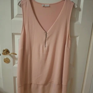 Ljusrosa ärmlös topp med dragkedja - Supersöt ljusrosa topp från Bodyflirt med v-ringning och silverfärgad dragkedja framtill. Toppen är ärmlös och har en snygg lager-på-lager-effekt nertill. Perfekt för dig som gillar en enkel men chic stil.