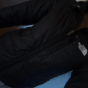 pufferjacka från The North Face - Säljer en svart pufferjacka från The North Face med huva och dragkedja. Jackan har en clean look med logga på bröstet och ett mönster med loggor på insidan som gör att man kan använda jackan då båda sätten🩷Perfekt för kalla dagar och riktigt snygg streetstil😇 den är S 