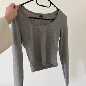 Grå croppad långärmad topp från Shein - En enkel och stilren grå croppad topp från Shein med lång ärm och rund halsringning. Tillverkad i mjukt och stretchigt material som sitter snyggt på kroppen. Perfekt att matcha med jeans eller kjol för en clean look.