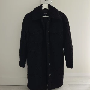 Svart teddykappa från vero moda - Mysig svart teddykappa med lång ärm och knappar framtill. Jackan har en rak och loose passform, perfekt för att hålla värmen under kyliga dagar. Endast använd ett fåtal ggr så den är som ny.Längd 91 cm💕