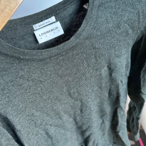Mörkgrön merinoullströja Lindbergh - Snygg mörkgrå långärmad tröja från Lindbergh i mjuk merinoull. Enkel och stilren design med rund halsringning och diskret logga på bröstet. Perfekt för lager-på-lager under kyliga dagar. Säljer den pga jag helt enkelt växt ur den och inte använder längre.