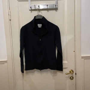 Svart merinoullskofta från These Glory Days - Säljer en svart kofta från These Glory Days i mjuk och lyxig merinoull. Koftan har hel dragkedja framtill och hög krage, perfekt för lager-på-lager. Enkel och stilren design som funkar till allt.