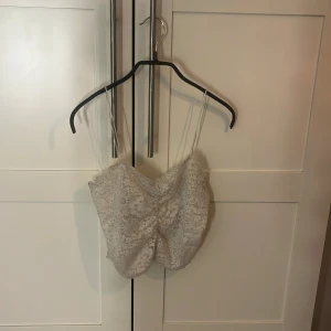 Vit spetsig linnetopp från BikBok - Supersöt vit linnetopp från BikBok med tunna axelband och blommig spets över hela toppen. Croppad modell med insydda kupor och mjukt innerfoder i satinliknande material. Perfekt att styla med jeans eller kjol för en fräsch look.